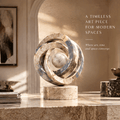 The Multi-Temporal Ring sculpture – five interlocking concentric marble arcs in alternating warm travertine and blue-grey marble with gold veining, central marble sphere, on cylindrical travertine plinth, full product front view in bright arched gallery with warm dappled sunlight